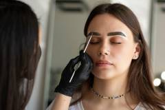 Eyebrow master paints a young woman with a paintbrush in a beauty salon